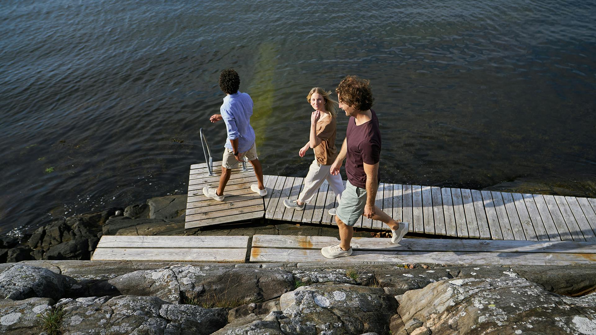 Three friends strolling on a dock by the water, enjoying a leisurely walk together.